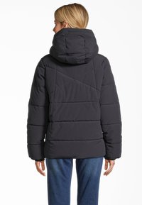Schwarze Steppjacke mit Kapuze, die ein gesteppter Design, horizontale Nähte und eine leicht lockere Passform aufweist. Sichtbare Ärmel und eine Umriss von Taschen.