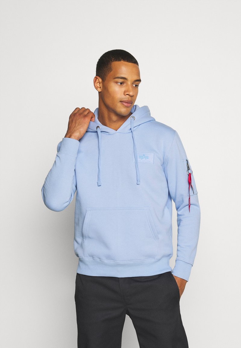 Felpa in cotone azzurro chiaro con tasca frontale, cappuccio con lacci e tasca laterale con zip dotata di un tirante rosso. Dettaglio del logo semplice sul petto.
