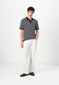 Striped polo skjorte med marineblå og grå vandrette striber, korte ærmer, knaplukning, samt brede hvide bukser og sort fodtøj.