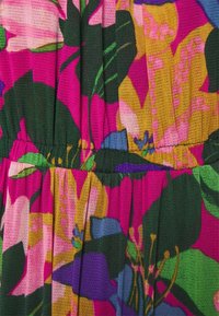 Tela brillante con grandes patrones florales abstractos en rosa, amarillo, verde, púrpura y azul, con costuras visibles y secciones fruncidas.