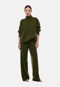 Pull-over en tricot vert olive avec un col haut, coupe décontractée et épaules tombantes, associé à un pantalon large assorti en tissu doux.
