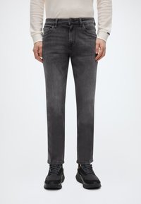 Γκρι τζιν παντελόνι denim με ευθεία γραμμή, πέντε τσέπες και λεπτή ξεθωριασμένη υφή. Συνδυασμένο με μαύρα αθλητικά παπούτσια.