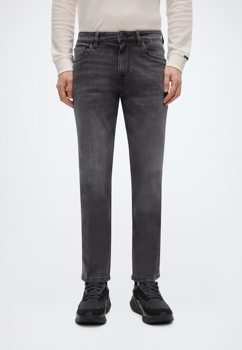 Γκρι τζιν παντελόνι denim με ευθεία γραμμή, πέντε τσέπες και λεπτή ξεθωριασμένη υφή. Συνδυασμένο με μαύρα αθλητικά παπούτσια.