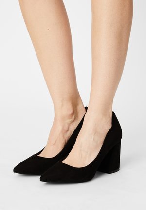 Zapatos de tacón alto de ante negro con punta afilada y tacón de bloque grueso. Textura suave con un diseño simple y elegante.