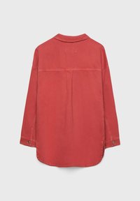 Camicia a maniche lunghe rossa sbiadita con bottoni vista da dietro, con una singola pince e polsini abbottonati su uno sfondo semplice.