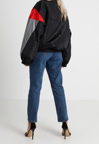 Giacca a vento nera, oversize, con dettagli rossi e grigi, polsini elasticizzati. Abbinata a jeans a vita alta blu e sandali neri con tacco alto.
