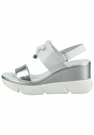 Hvid og sølvfarvet kilehælssandal med åben tå, justerbar ankelrem og dekorativ knude på frontrem.