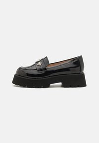 Mocasini din piele lustruită neagră, cu o talpă platformă groasă, texturată, de culoare neagră și detalii decorative din metal argintiu pe față.