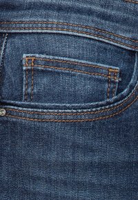 Mørkeblå denimjeans med en baklomme med oransje broderi og en metallnitte. Glatt tekstur med et subtilt falmet mønster.
