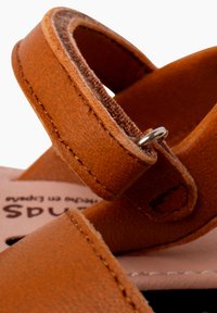 Sandali in pelle marrone con cinturino regolabile e hardware in argento, soletta morbida e dettagli di cucitura sulla tomaia.