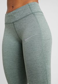 Gröna träningsbyxor gjorda av texturerat tyg, med hög midja, sömlös design och en liten silver Nike-logga på låret.