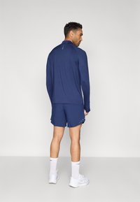 Μπλε ναυτικό τοπ με μακριά μανίκια και ταιριαστό σορτς από ελαφρύ ύφασμα, με διακριτικές λεπτομέρειες, φορεμένα με λευκά αθλητικά παπούτσια και καλτσάκια μέχρι το γόνατο.