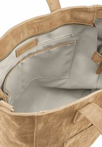 Interieur van handtas van cognackleurig suède met een gladde lichtgrijze voering, voorzien van een ritssluiting en een open vak voor opslag. Eenvoudig ontwerp.