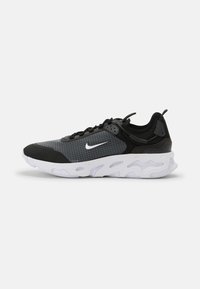Fekete és szürke sportcipő, textúrált hálós felsőrésszel, rácsos mintával, fehér Nike logóval és vastag, párnázott talppal.
