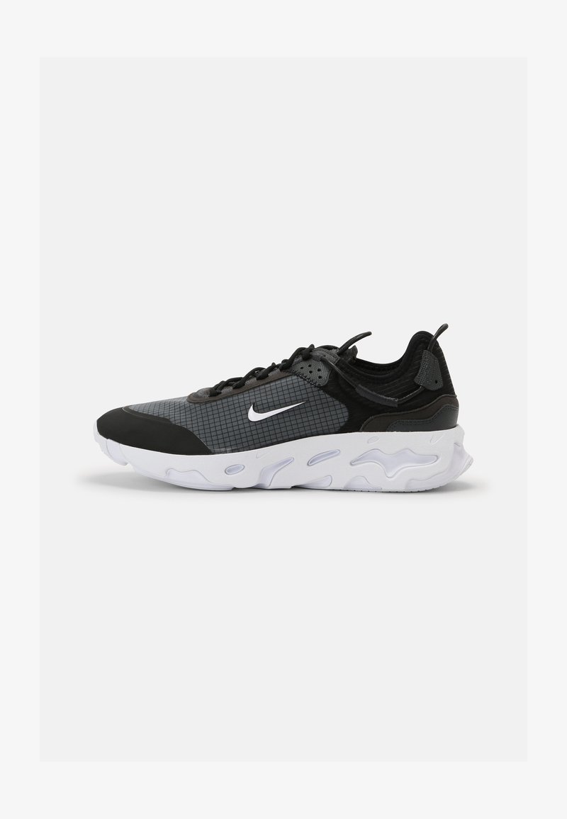 Mustat ja harmaat urheilujalkineet, joissa on tekstuuripintainen verkko-osa, ruudukkomalli, valkoinen Nike-logomerkki ja paksu, pehmustettu pohja.