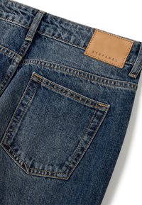 Jeans en denim bleu foncé avec des coutures visibles, une étiquette en cuir portant la mention "STEFANEL" et une seule poche arrière au design classique.