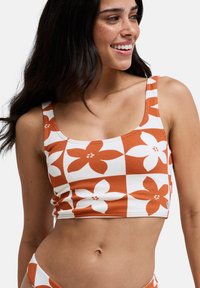 Oranžovo-biely kvetinový vzorovaný crop top so štvorcovým dizajnom, textúrovanou látkou a širokými ramienkami. Má priliehavý strih a bočné nariasenie.