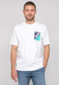 T-shirt en coton blanc avec un design de poche graphique représentant un palmier coloré, à manches courtes et col rond. Coupe décontractée, texture lisse.