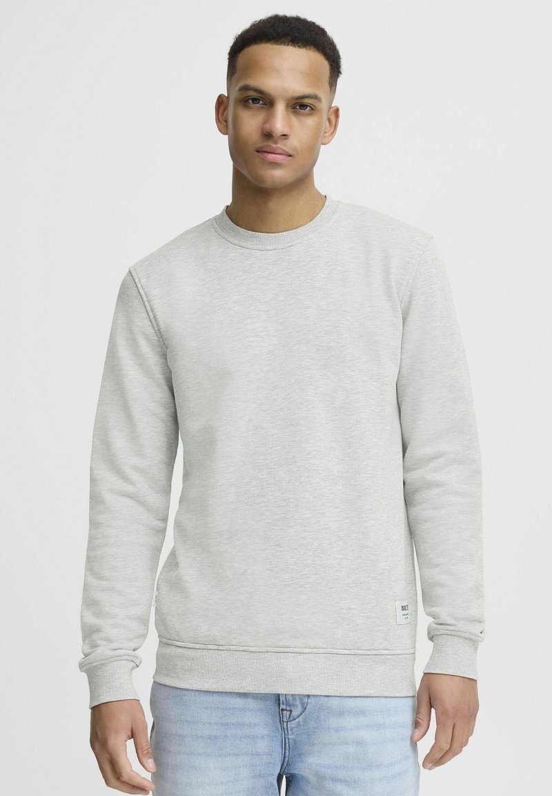 Light grey sweatshirt with a round neckline, ribbed cuffs, and hem. Slight texture and a small branded label at the bottom left.