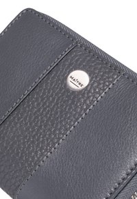 Portefeuille en cuir gris présentant des panneaux texturés et lisses, un détail de couture et un accent logo argenté. Design compact avec un matériau durable.