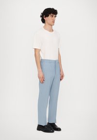 Vaaleanbeige t-paita yhdistettynä vaaleansinisille raidallisille housuille. Housuissa on räätälöity istuvuus ja niitä käytetään mustien kenkien kanssa.