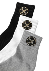 Tres pares de calcetines acanalados en negro, blanco y gris. Cada uno presenta un logo circular con fondo negro y bordado en dorado.