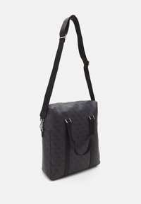 Sac en tissu synthétique noir à texture à motifs, avec deux poignées supérieures, une bandoulière réglable et des garnitures en métal argenté.