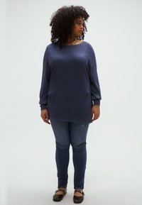 Μπλε σκούρο ριγέ μπλούζα με μακριά μανίκια και άνετη εφαρμογή, συνδυασμένη με σκούρο τζιν και μπλου flats. Λείο ύφασμα με ραβδωτή υφή.