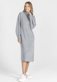 Szary, dzianinowy sweter z kołnierzem typu turban, z długimi rękawami, luźny krój i długość do połowy łydki, zestawiony z białymi sneakersami na grubej podeszwie.