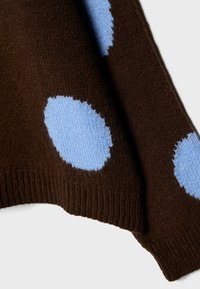 Hnedý sveter s veľkými svetlomodrými bodkami, vyrobený z jemnej pleteniny s rebrovaným lemom a hladkou textúrou.