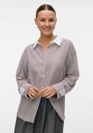 Chemise à rayures rouge et blanche avec un col blanc, manches longues et détails aux poignets ; portée avec une jupe grise.