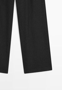 Schwarze Nadelstreifenhose mit geradem Schnitt. Der Stoff weist eine dezente Textur auf und kontrastierende weiße vertikale Streifen. Sauberer Saumabschluss.