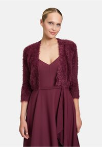 Cardigan court en laine moelleuse de couleur bourgogne avec des manches trois-quarts ; porté par-dessus une robe à décolleté en V profond assortie. Surface texturée et matériau doux.