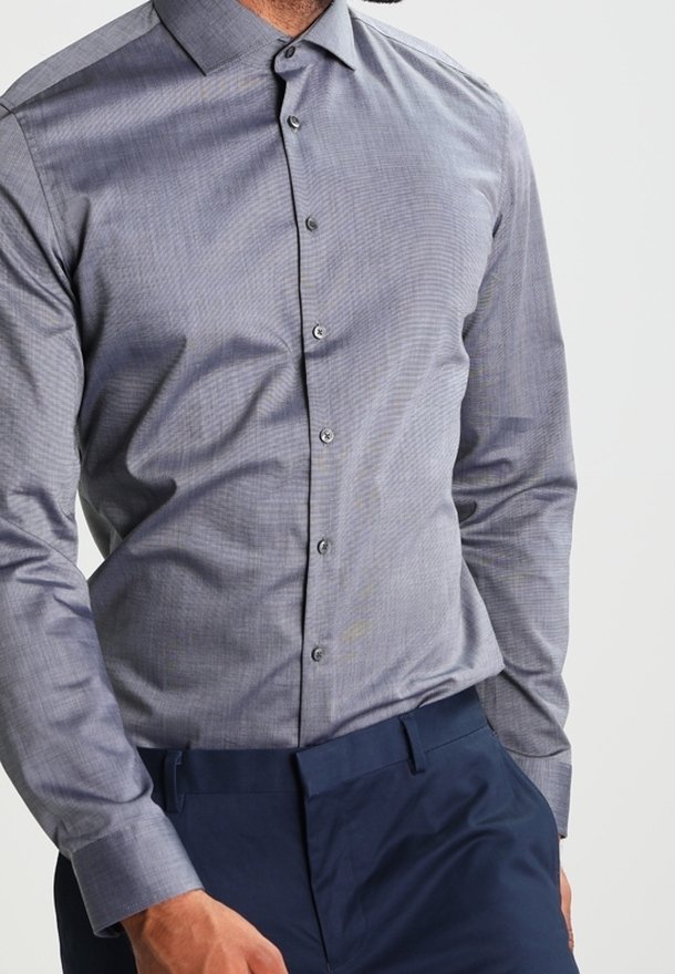 Grijs, gestructureerd overhemd met knoopsluiting en een geruit patroon; heeft een kraag en lange mouwen, gecombineerd met donkere broek.