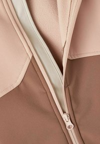 Mit einem Reißverschluss versehene Jacke aus einer Kombination von sanftem Pink und beige-stoff, mit einer glatten Textur und einer kontrastierenden Fütterung, die in der Nähe des Reißverschlusses sichtbar ist.