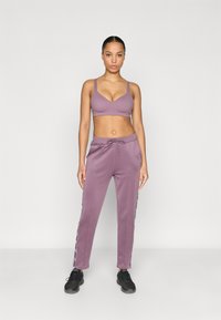 Μωβ αθλητικό σουτιέν και ταιριαστά παντελόνια φόρμας με πλαϊνές λεπτομέρειες. Τα παντελόνια διαθέτουν κορδόνι στη μέση, λεία υφή και στενές γραμμές στα πόδια.