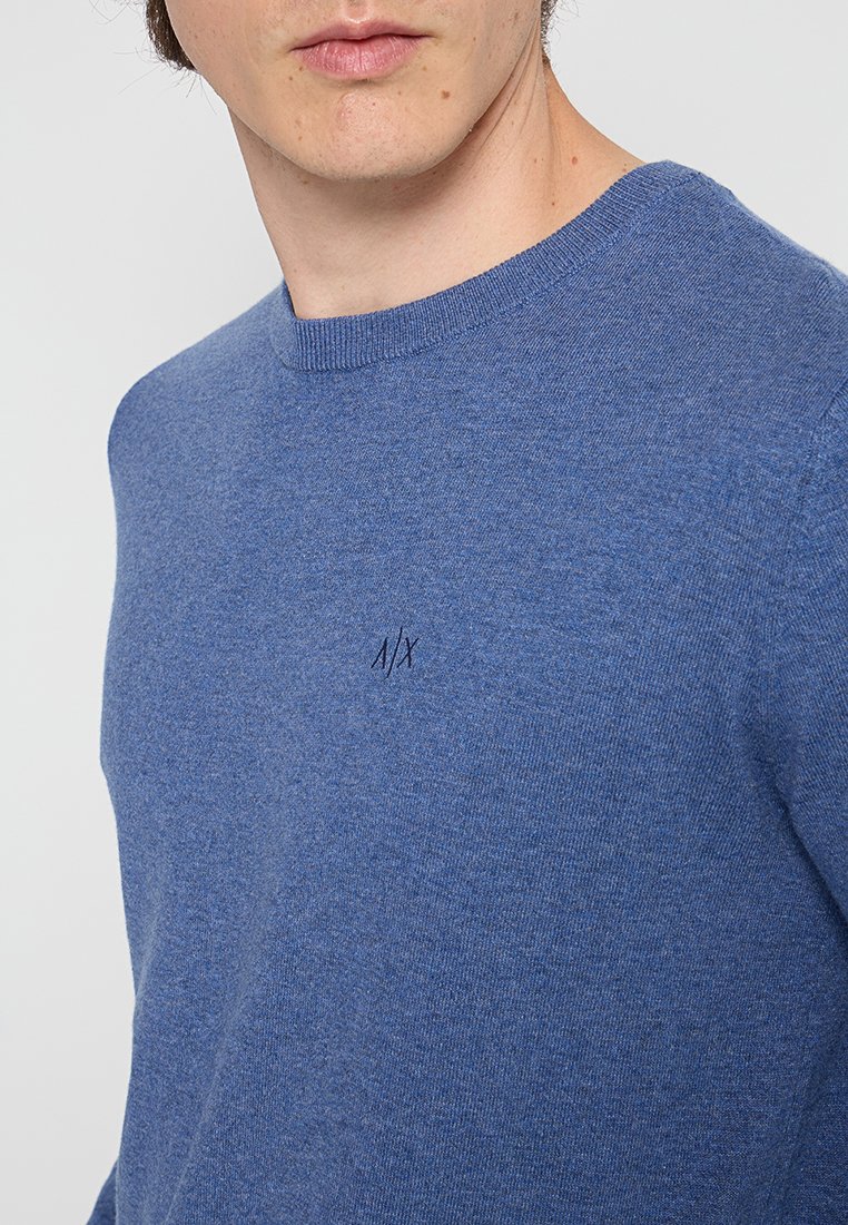 Blauer Pullover aus weichem Material, mit Rundhalskragen und einem kleinen gestickten Logo über der linken Brust.