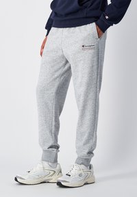 Grijze fleece sweatpants met elastische tailleband, zijzakken en geborduurd "Champion Athletic Wear" logo. Ribgebreide boorden bij de enkels.