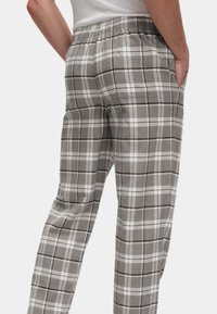 Grijze geruite pyjamabroek met een elastische tailleband. Heeft een zachte textuur, een wit en zwart ruitpatroon en zijzakken.