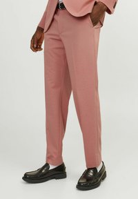 Svetlo roza krojene hlače iz gladkega materiala, s slim fit krojem in stranskimi žepi, v kombinaciji z črnimi čevlji loafers in belimi nogavicami.