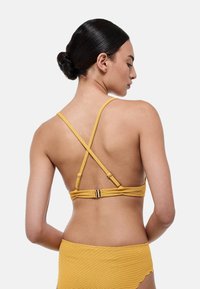 Bralette jaune à côtes avec des bretelles croisées réglables et un fermoir en ton doré à l'arrière, avec un matériau texturé et un design minimaliste.