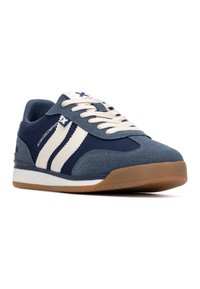 Zapatilla deportiva azul marino con rayas blancas, parte superior de ante y tela texturizada, y suela de goma. Presenta punta redondeada y diseño de cordones.
