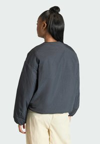 Tmavošedý nadrozmerný sveter s dlhými rukávmi, okrúhlym výstrihom a textúrovanou tkaninou, nosený s svetlými nohavicami, zobrazený zozadu.