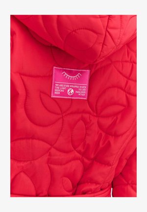 Červená prešívaná bunda s kapucňou a výraznou ružovou štítkom s textom. Tkanina má hladkú, jemnú štruktúru s jemným vzorom.