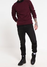 Vinröd tröja med raglanärmar, kombinerad med svarta slitna jeans med uppspruckna knän, och svarta snörkängor.