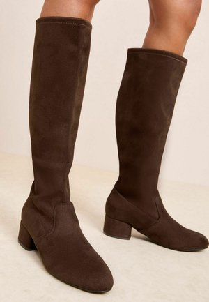 Bottes marron montantes en suede souple, avec un talon carré et un design lisse et sans couture sans attaches visibles.