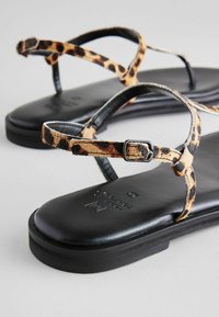 Sandále s leopardím vzorom a čiernymi koženými podrážkami, s tenkými krížovými popruhmi a kovovou prackou na nastavenie, minimalisitcký dizajn.