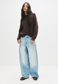 Maglione a coste marrone, jeans a gamba larga blu chiaro con tasche laterali e scarpe nere con stampa leopardata. Design semplice con vestibilità comoda.