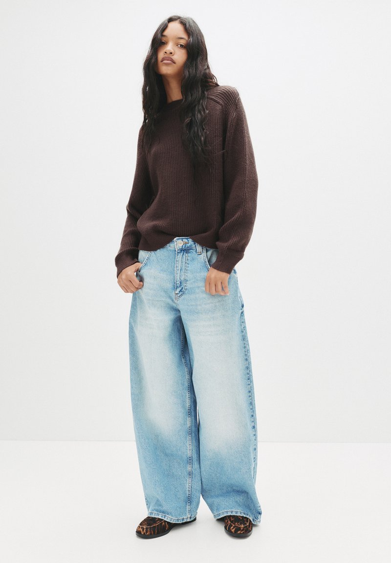 Maglione a coste marrone, jeans a gamba larga blu chiaro con tasche laterali e scarpe nere con stampa leopardata. Design semplice con vestibilità comoda.