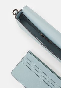 Jasnoniebieski portfel wykonany z teksturowanego materiału, z kieszenią na zamek, miejscami na karty oraz ciemną lamówką. Widok otwarty pokazuje wnętrze wyściełane materiałem.